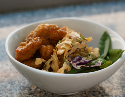 Bowl of oven baked breaded chicken wings in creamy sauce over bed of rice, snow peas and slaw 