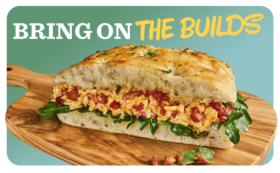 A bacon pimento cheese sandwich on focaccia bread resting on a wooden cutting board 
