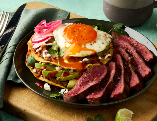 Grilled steak with a tostada topped with beans, avocado, egg, queso fresco, and pickled onions