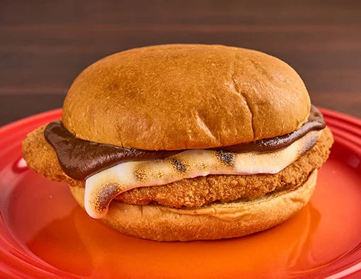 Crispy chicken filet with chocolate mole and bruléed marshmallow fluff on brioche bun, on a red plate