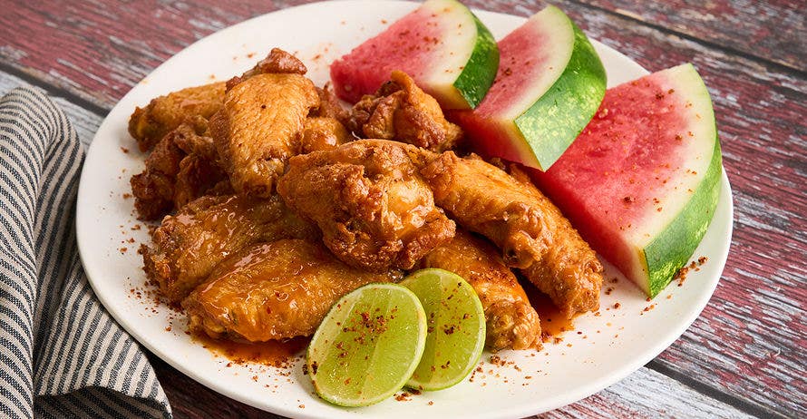 Chicken wings with tamarind glaze, served with chili lime watermelon and lime wedges on a white plate