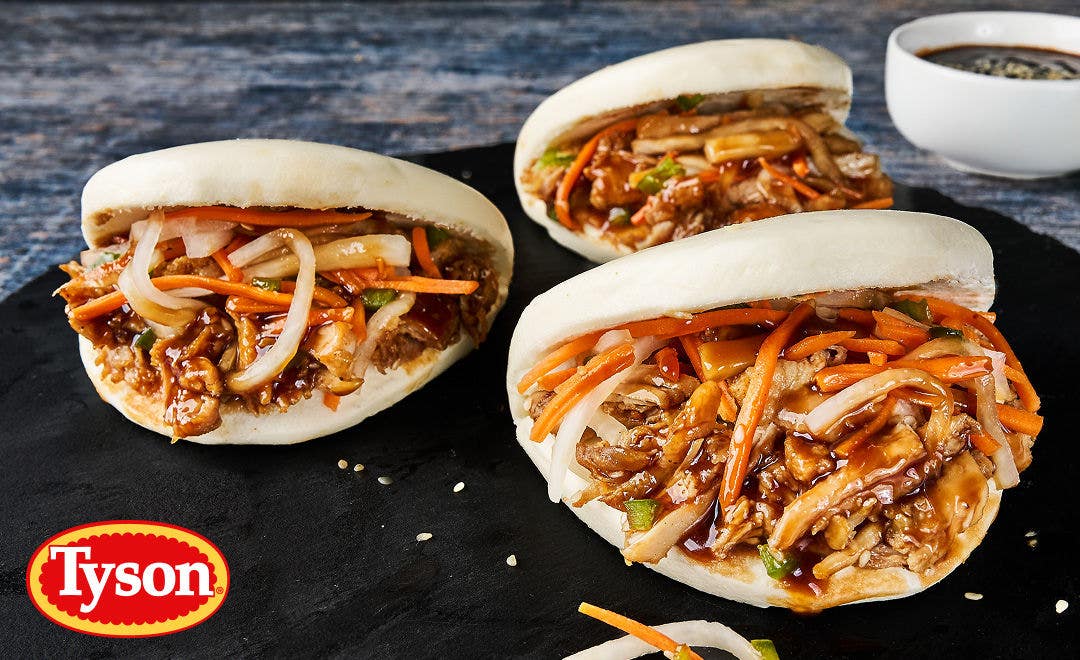 Three small bao buns stuffed with sauced, pulled chicken, daikon, carrots and sesame seeds 