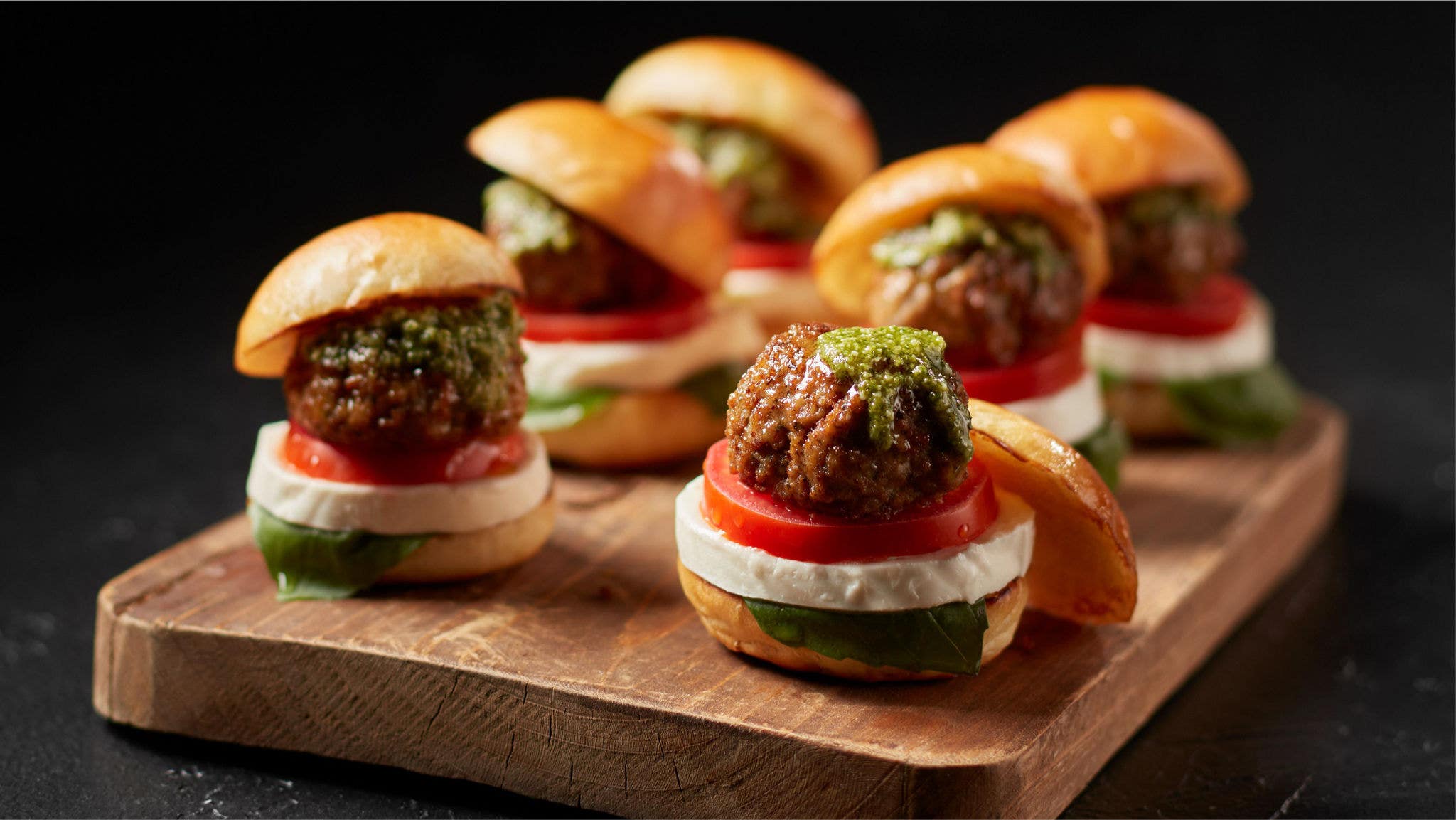 Six caprese meatball sliders plated on a cutting board