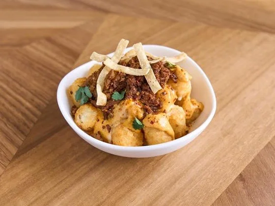 Golden tater tots topped with beef taco meat, nacho cheese, Aji Amarillo sauce, cilantro, and tortilla strips