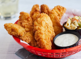 A red basket of fried chicken tenders with dipping sauce and pasta salad