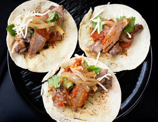 Smoked beef chuck shoulder roast covered in barbacoa sauce on a slightly toasted corn tortilla with onions and cilantro on a black plate