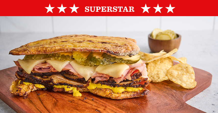 A pressed Cuban sandwich on a wooden board with chips and pickles