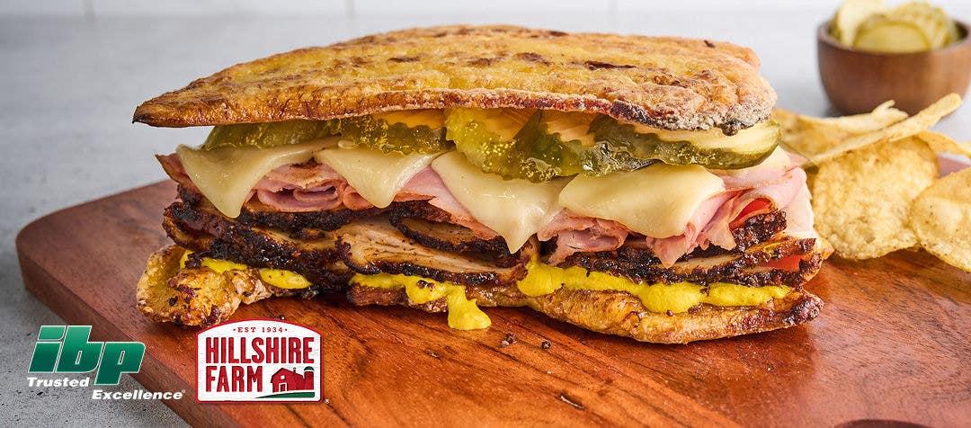 a sandwich stacked with pulled pork, ham, cheese, pickles and mustard between two large fried plantains