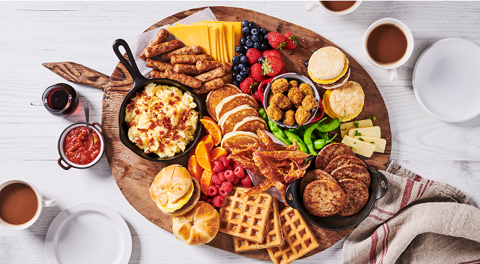 An overhead view of a large brunch board with pancakes, waffles, eggs, sausage, and fruit
