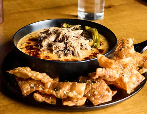 A skillet of creamy dip topped with pulled pork, served with crispy wonton chips