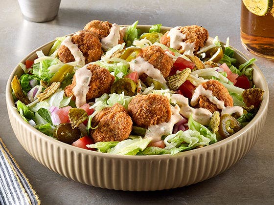 This bowl of  lettuce, topped with spicy breaded beef bites,  diced tomatoes, red onions, shredded pepper jack cheese, pickled jalapeños, a creamy jalapeño popper sauce and topped with crunchy jalapeño strips. 