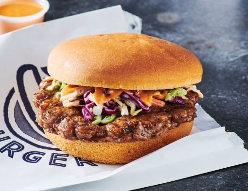 Beef burger patty on a whole grain bun with cucumber and pickled Asian slaw 