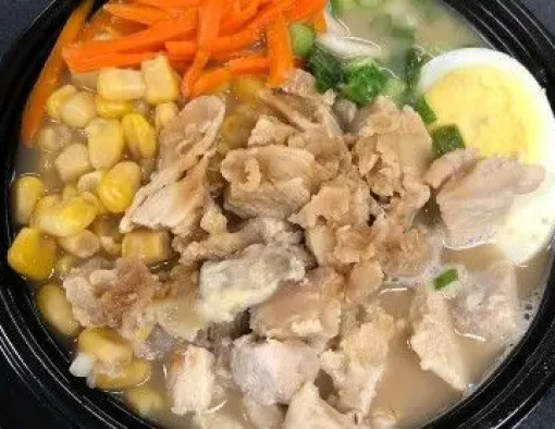 Bowl of broth and diced chicken with ramen noodles, corn, shredded carrots and half of a hard-boiled egg