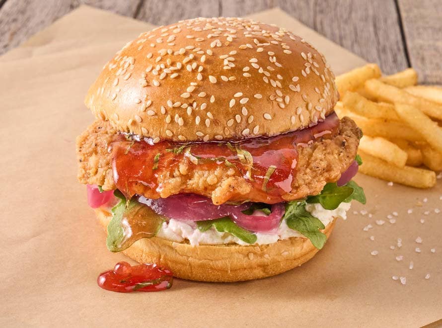 Crispy filet with goat cheese, jam and onions in a brioche bun on butcher paper with a side of French fries 