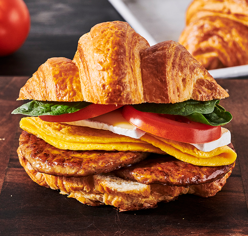 A toasted croissant with egg, mozzarella cheese, tomato and fresh spinach. 
