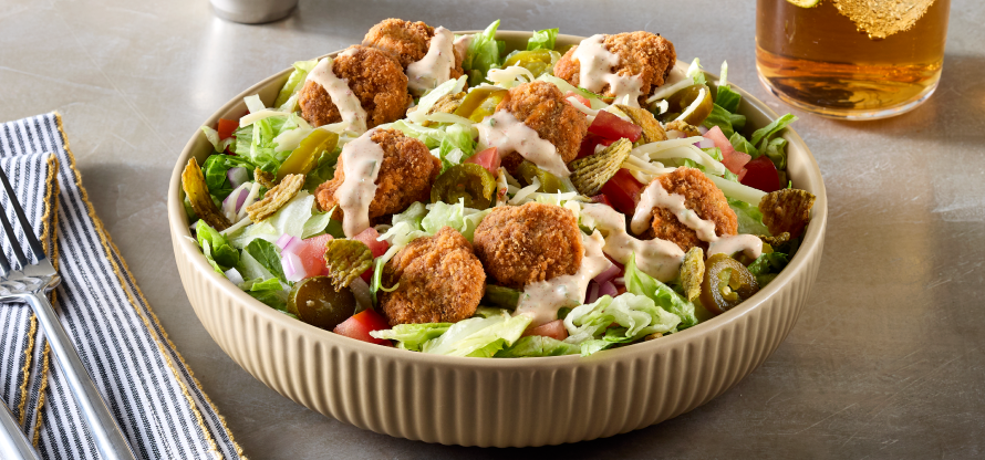 large salad of lettuce, various vegetables and breaded beef chunks with a drizzle of salad dressing