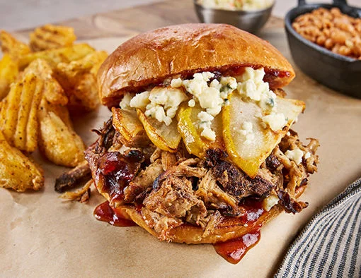 Fall pulled pork sandwich with cranberry-honey BBQ sauce, roasted pears, and blue cheese crumbles on a toasted potato bun