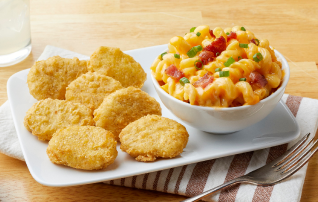 A plate of chicken nuggets next to a bowl of bacon mac and cheese
