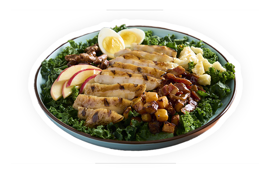 Grilled chicken breast filets over a plate of greens with eggs and apples