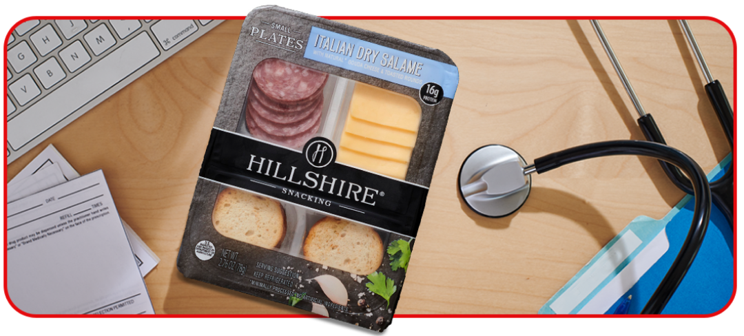 A package of crackers, sliced sausage and cheese sitting on a desk alongside a stethoscope and computer keyboard