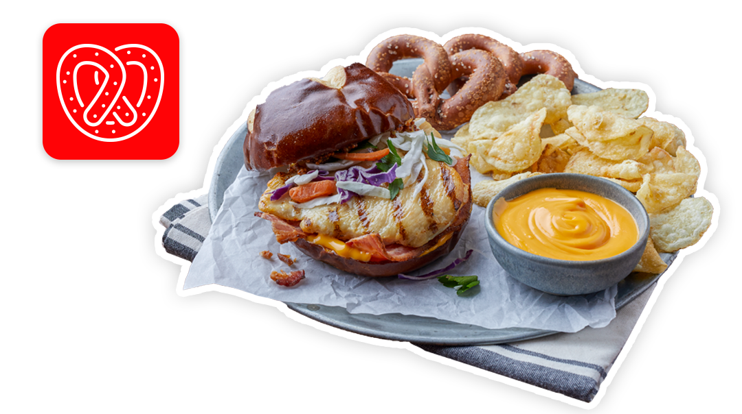 Grilled chicken sandwich on pretzel bun with chips, pretzels, and cheese sauce