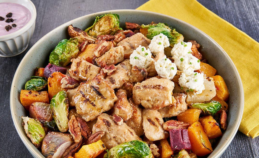 Overhead view of a bowl of roasted vegetables, Brussels sprouts, chicken chunks, cheese and whole pecans