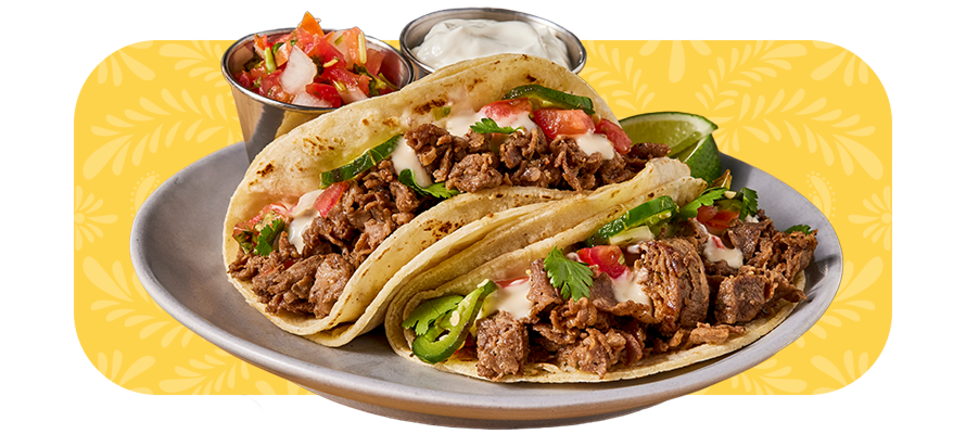 two loaded sliced beef tacos with sides of Pico de Gallo sauce and sour cream