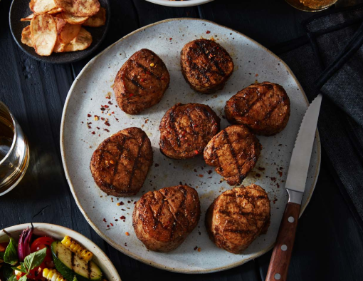 Spiced and grilled pork tenderloin medallions on a plate next to a drink