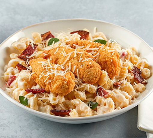 Mac and cheese topped with chicken tenders, bacon, Parmesan, and sliced scallions in a white bowl