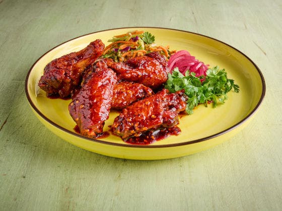 Red-sauced chicken wings on a yellow plate with coleslaw, pickled red onions, and cilantro