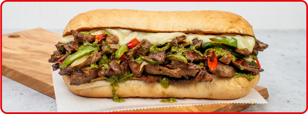 A footlong Philly cheesesteak sandwich loaded with peppers and topped with melted cheese. 