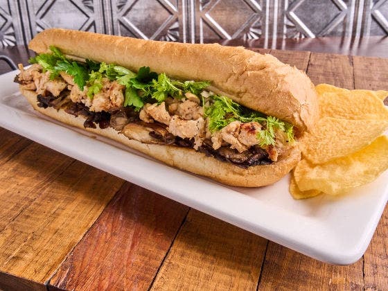 Chicken sandwich with black trumpet mushrooms, marsala vinaigrette on a hoagie roll, on a white plate