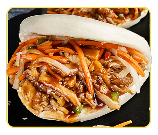 A small bao bun stuffed with chicken, pickled carrots and daikon with a second bun in the background 