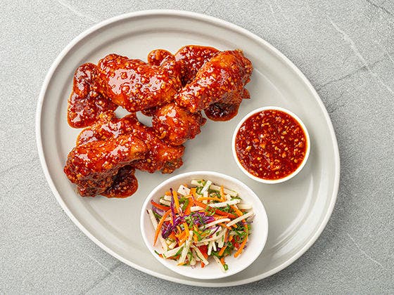 Bone-in chicken wings in hot honey hibiscus BBQ sauce with jicama slaw on a white plate