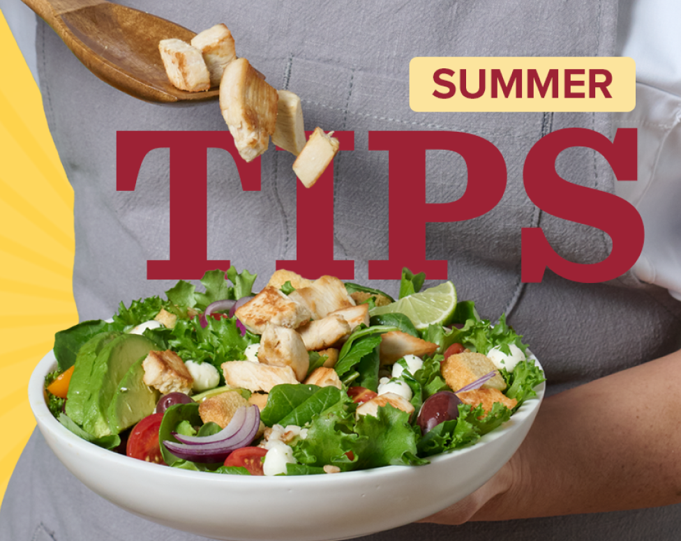 chef’s hands holding a white bowl with salad and adding roasted chicken from wooden spoon