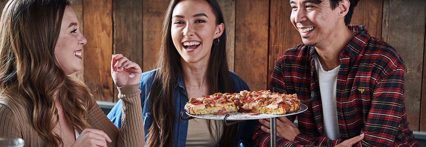 A group of friends sitting at a table and eating pizza at a restaurant. 