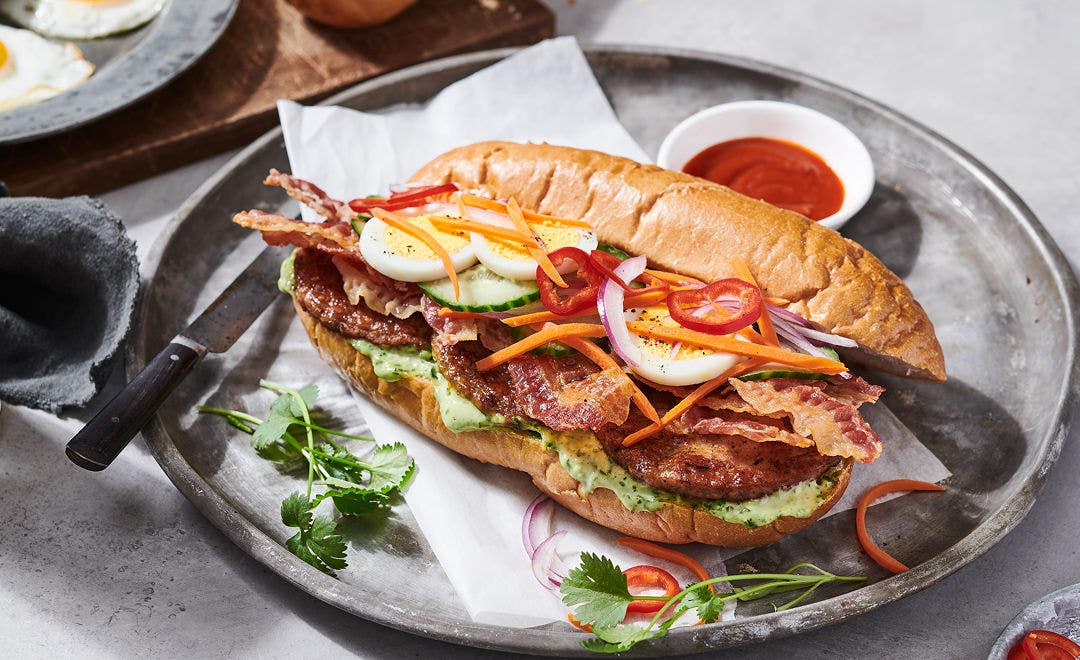 hoagie roll stuffed with sausage patties, bacon, sliced hard-boiled eggs with a side of sauce