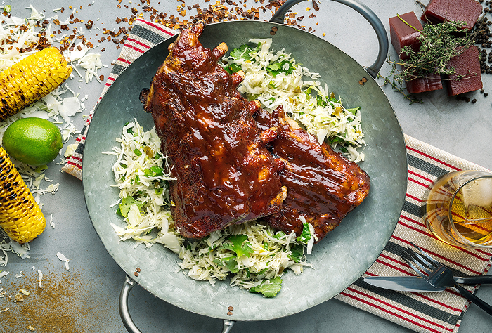 Delicious glazed BBQ ribs served on fresh cabbage salad with grilled corn and lime on the side