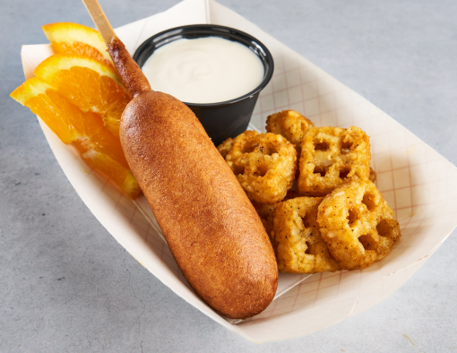 A paper to-go container with a turkey sausage pancake stick, a side of hashbrowns, dipping sauce and orange slices 