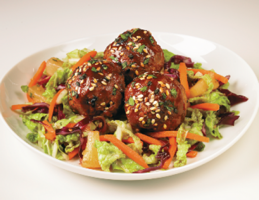 Bowl of beef meatballs covered in teriyaki, sesame seeds and tossed with pineapples, shredded carrots and lettuce 