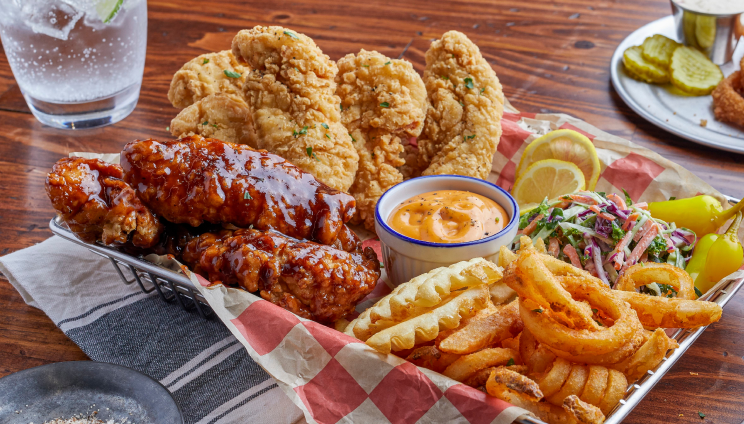Basket of fried chicken tenders, wings, waffle fries, onion rings, coleslaw, sauce, lemon wedges