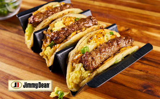 A taco holder with three pancake tacos filled with sausage links, scrambled eggs and chives  