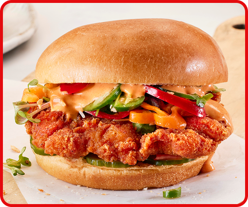 A plated breaded chicken sandwich with fresh vegetables on a bun