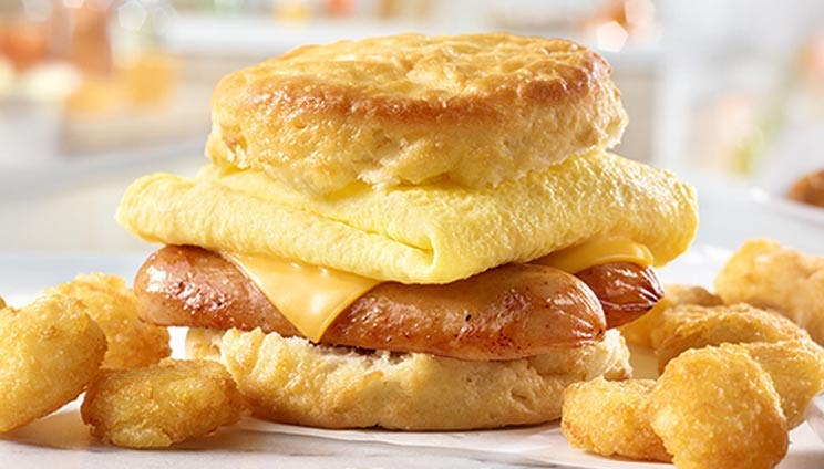 A sausage, egg, and cheese biscuit sandwich served with a side of golden-brown tater tots