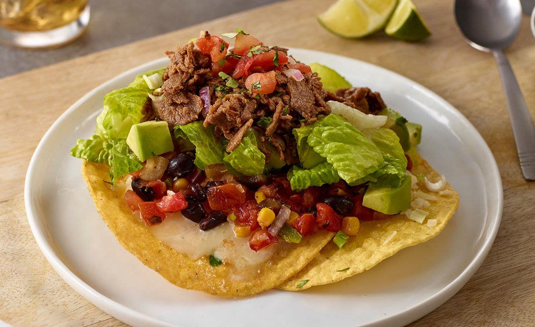 two tostada shells loaded with pico de gallo, black beans, melted cheese, diced avocado and sliced beef