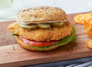 Fried chicken sandwich with pickles, lettuce, tomato on seeded bun; chips on wooden board