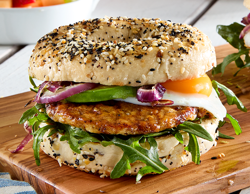 Hearty everything bagel sausage sandwich with egg, avocado, and arugula.