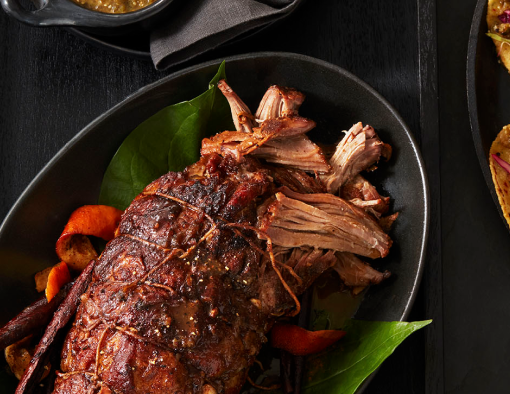 Pork carnitas on a plate next to a carnitas taco with cilantro and jalapeno