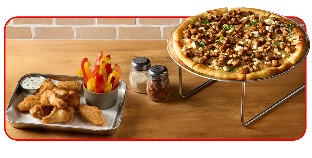 Overhead shot of pizza and side of wings on table setting