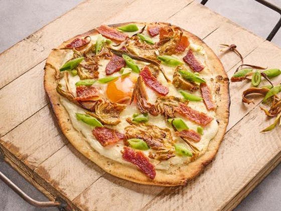 Brunch flatbread featuring Hickory Smoked Honey Thick Cut Bacon, ricotta, fried artichokes, spring peas, and sunny-side-up egg